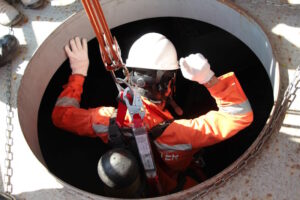 Worker wearing safety equipment being lowered by ropes into an industrial hole