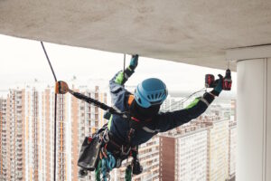 worker hanging with a rope and harness working with a power drill hanging under a ledge.